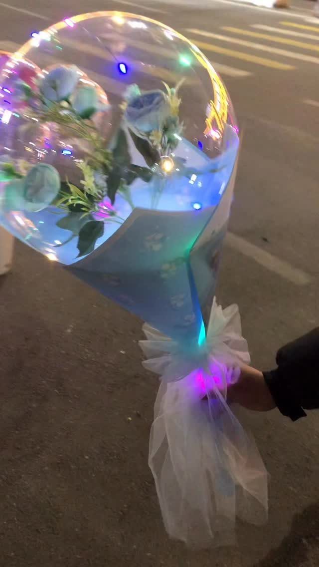 Clear balloon bouquet with blue flowers and colorful LED lights held at night