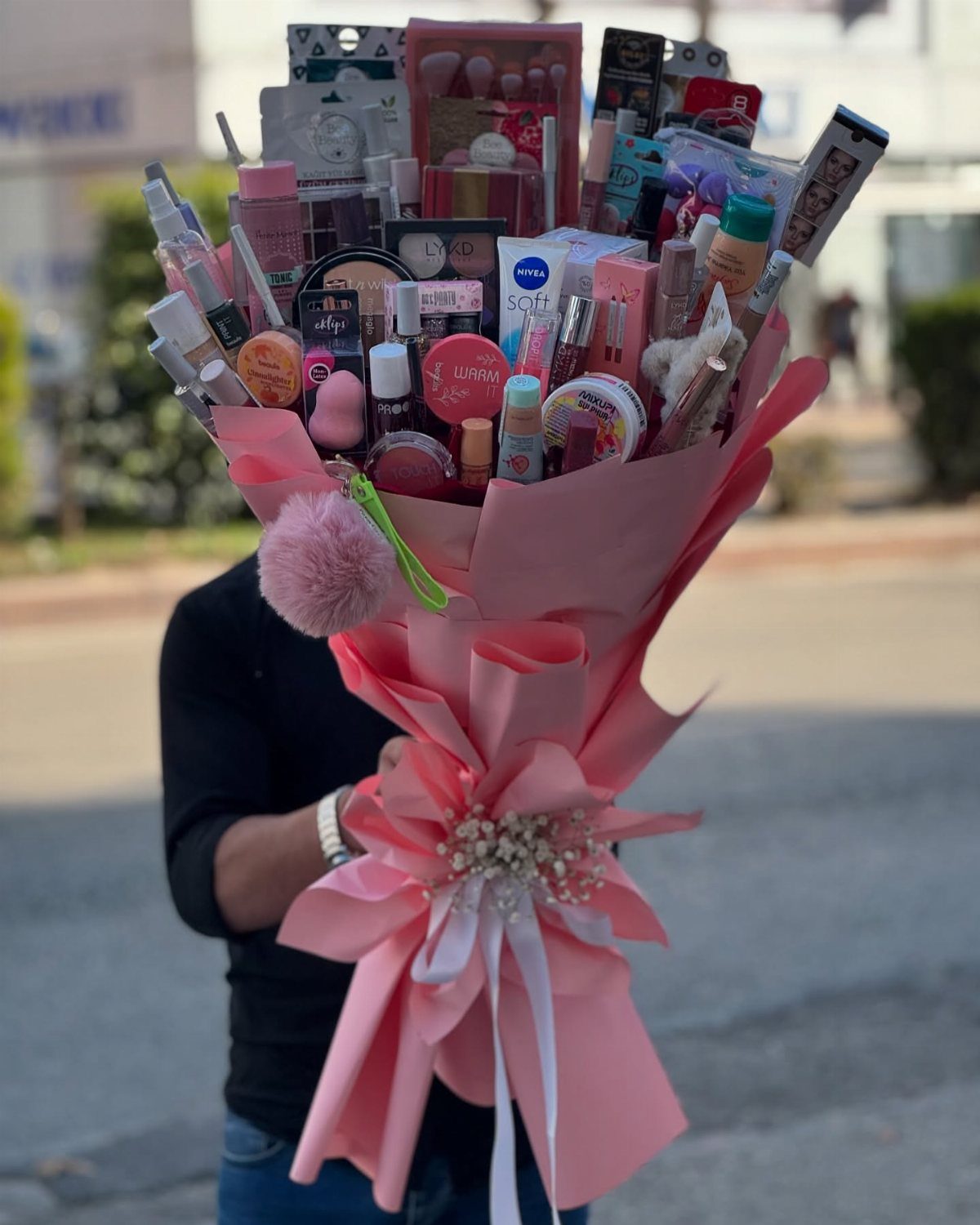 Makeup bouquet wrapped in pink paper containing various cosmetics and beauty products.