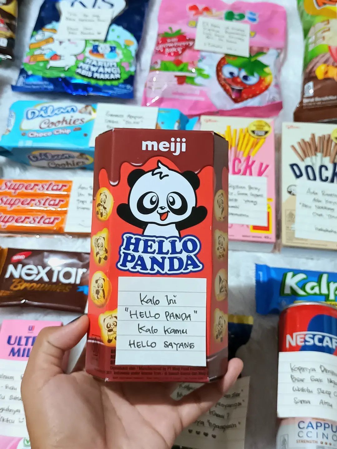 Hand holding a Hello Panda snack box with a handwritten note among candies.
