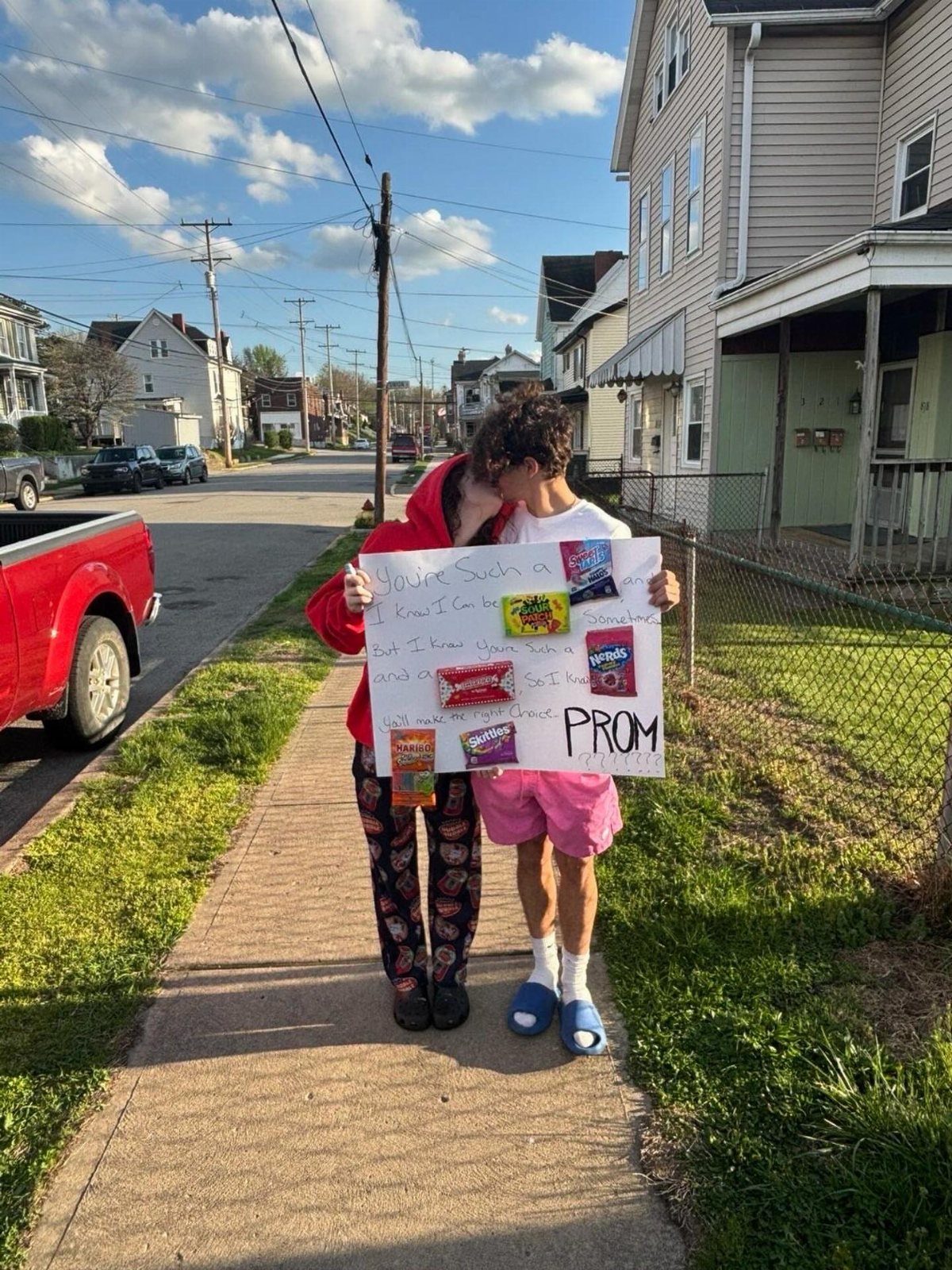 Couple kissing while holding a promposal poster decorated with various candy bars.