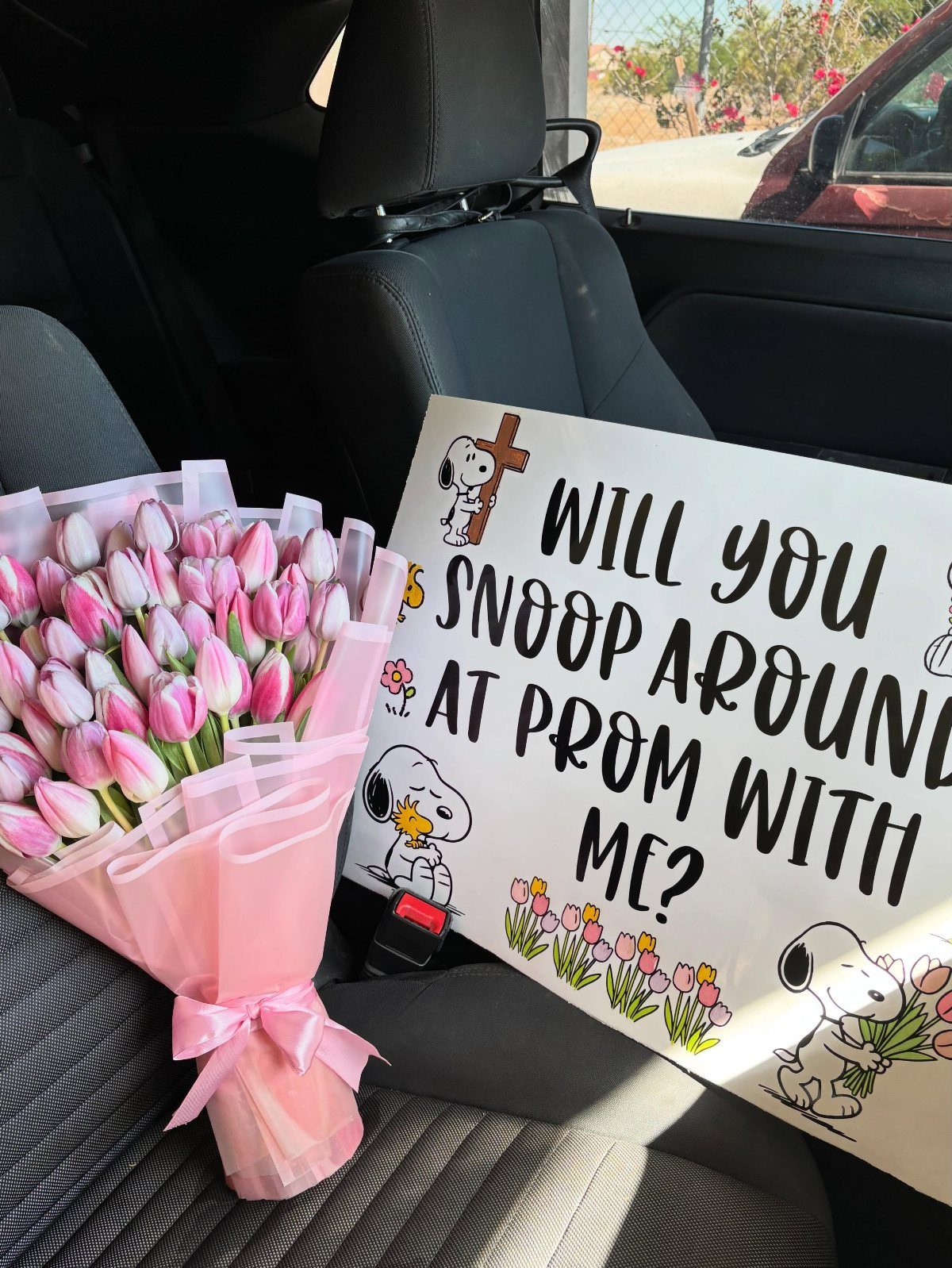 Snoopy themed promposal sign and pink tulips on a car seat