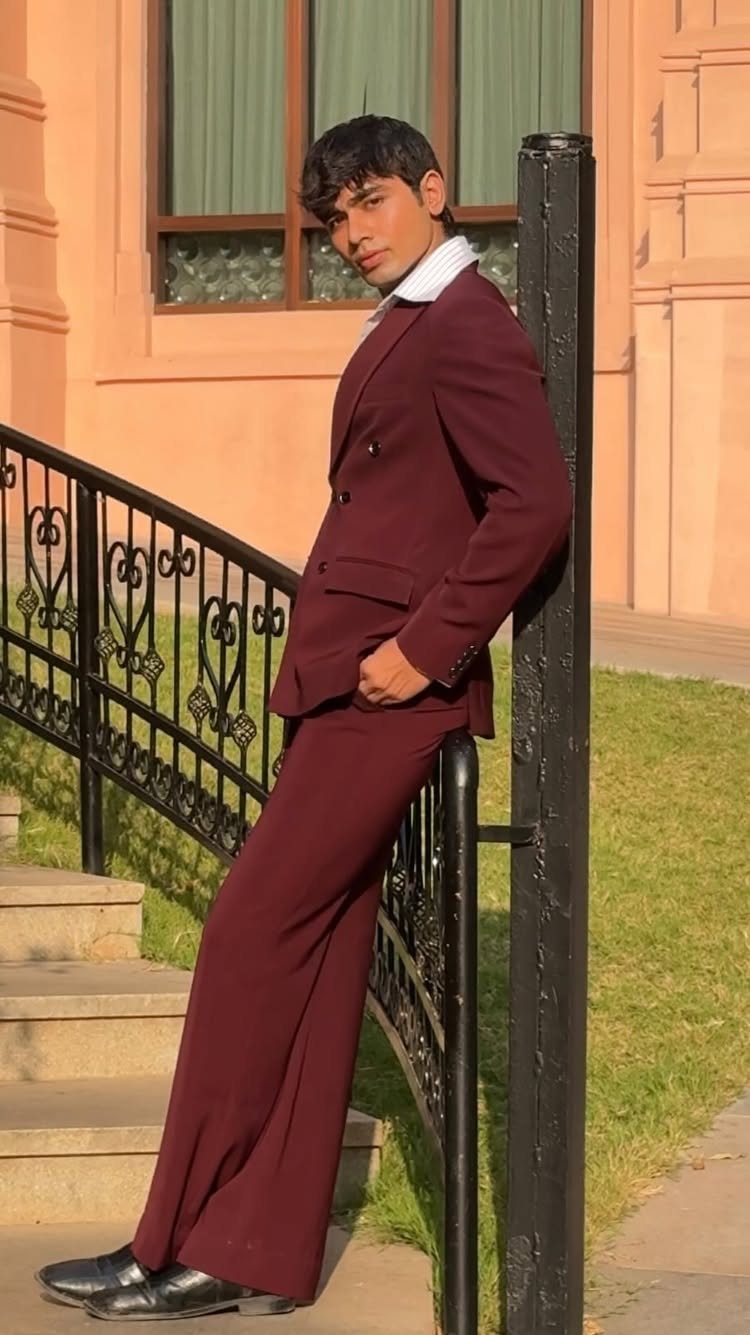Young man in a dark red suit leaning against a black metal railing.