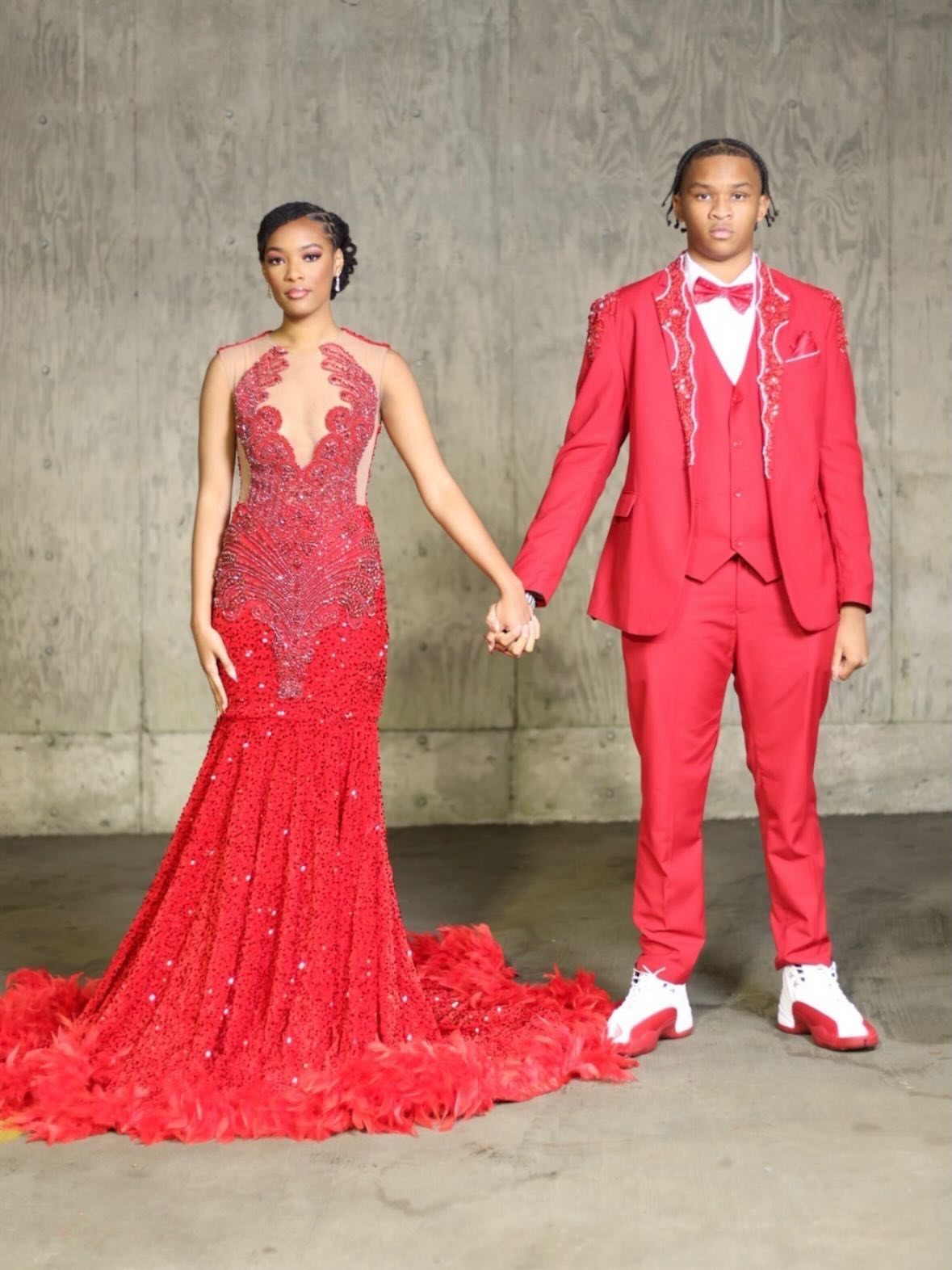 Couple holding hands wearing matching red formal attire against a grey wall