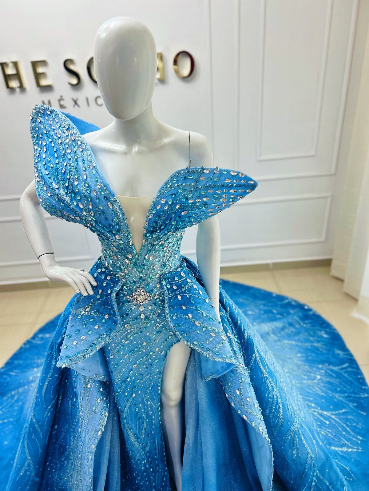Bright blue sequined gown with wing-like shoulders on a white mannequin