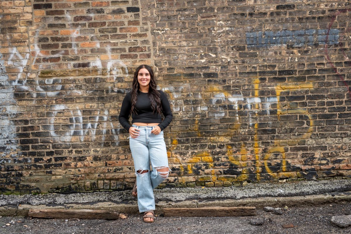 Young woman posing in front of a weathered brick wall with graffiti.