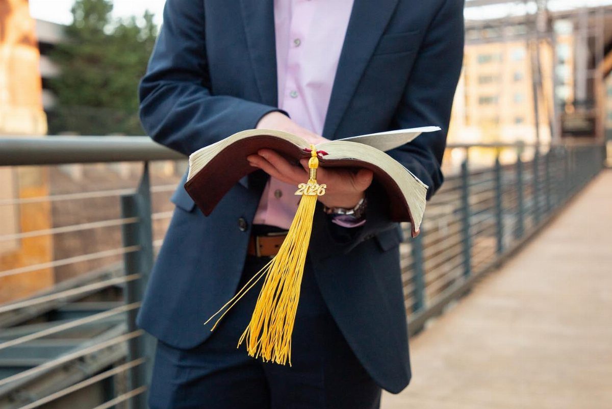 Person in a blue suit holding an open book with a yellow tassel.
