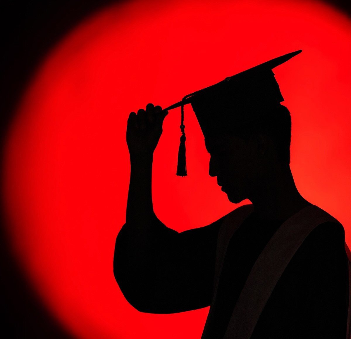Graduation silhouette of a student in cap and gown against red backlighting