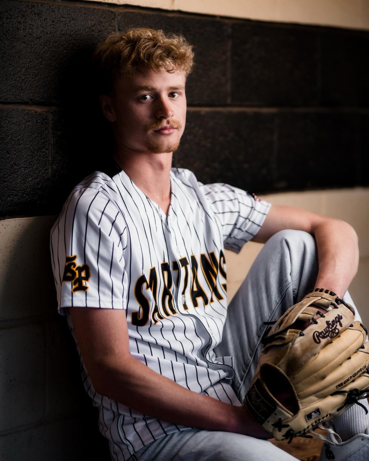 Young man in a pinstriped baseball uniform holding a glove against a brick wall