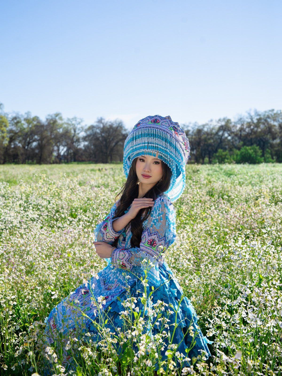 Woman in blue traditional cultural attire posing in a field of white wildflowers.