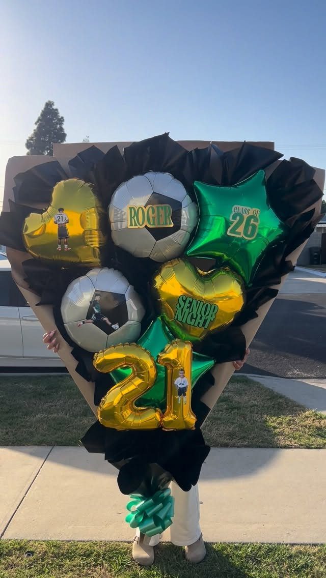 Person holding a large bouquet of gold, green, and soccer ball balloons.