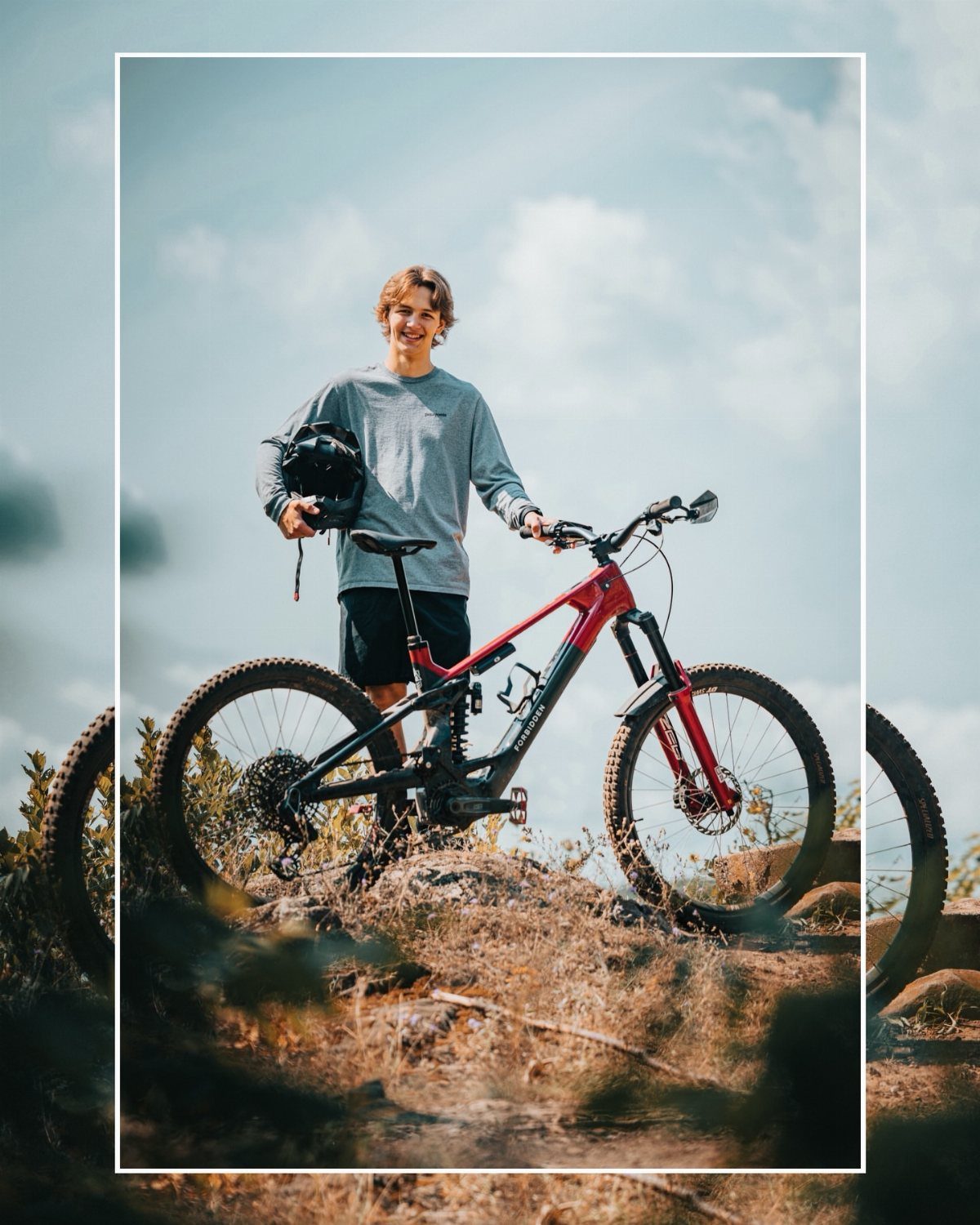 Young man posing with a red mountain bike on a rocky hillside.