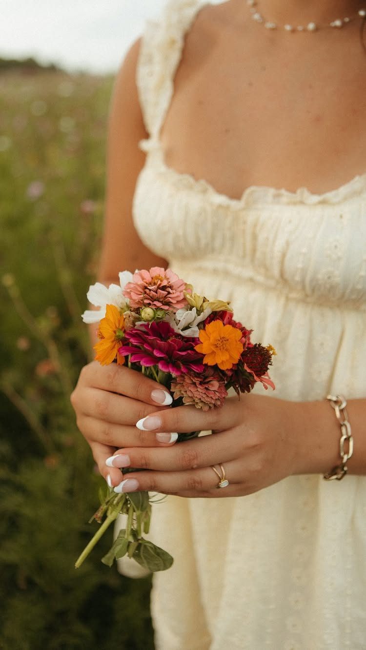 Person in a cream dress holding a colorful flower bouquet in a field