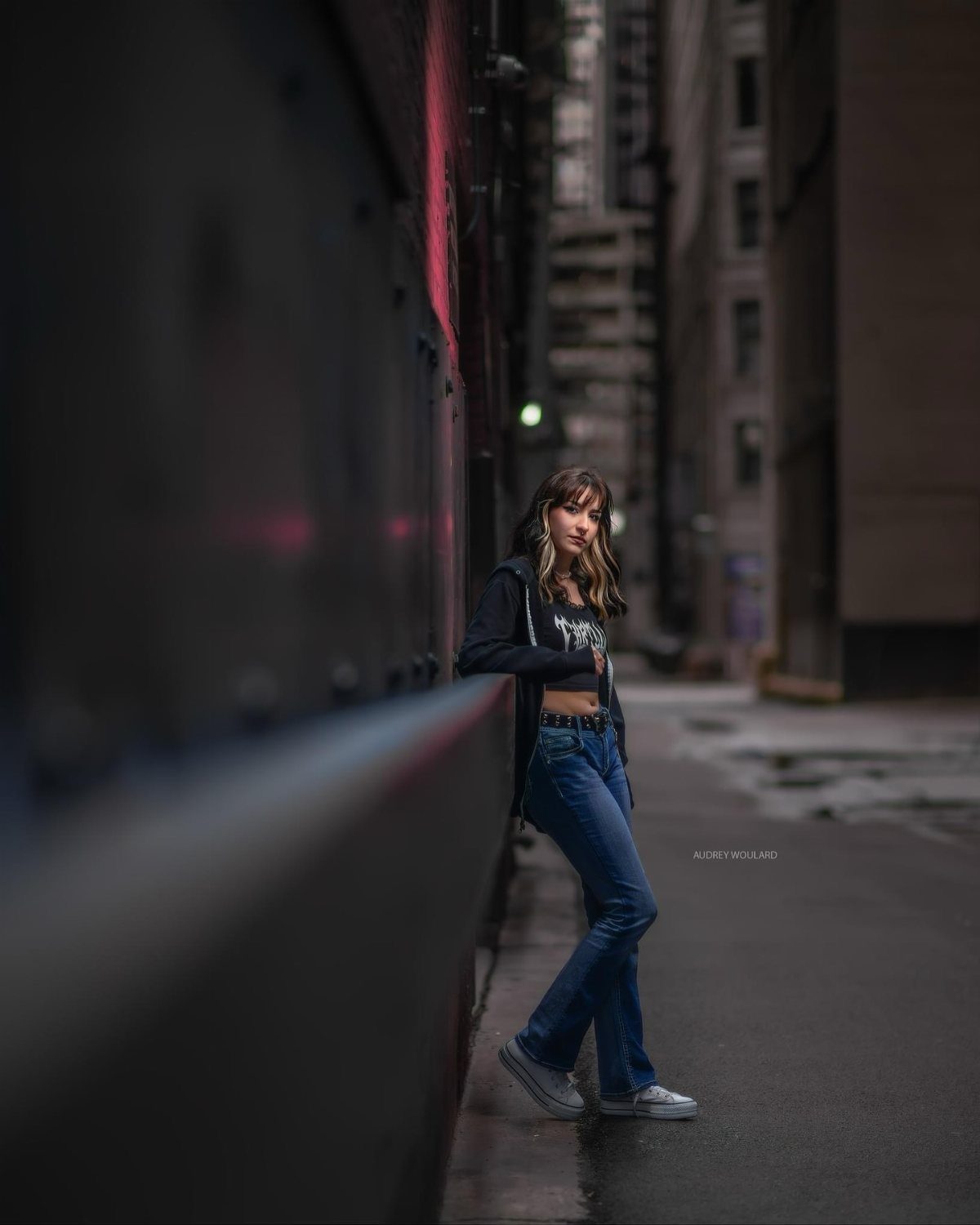 Young woman in a black hoodie and flare jeans posing in a city alley