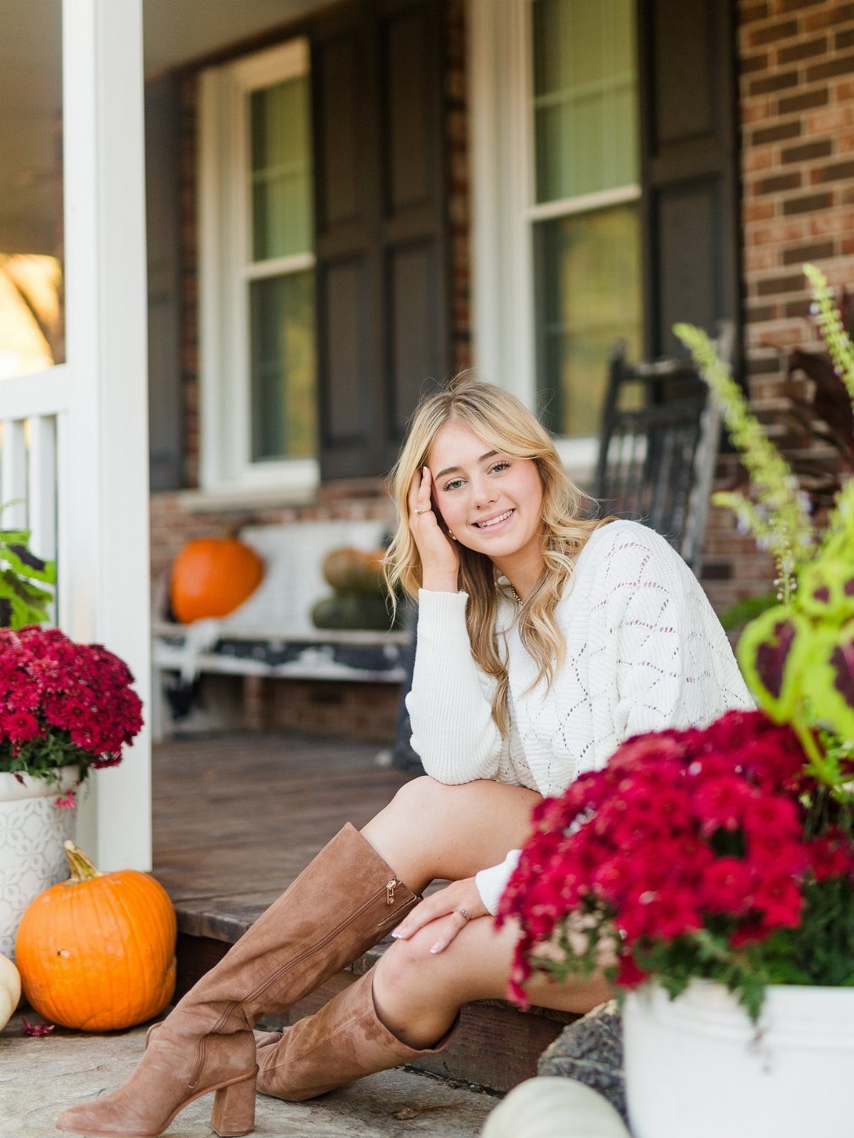 Young woman in white sweater and brown boots sitting on a decorated porch