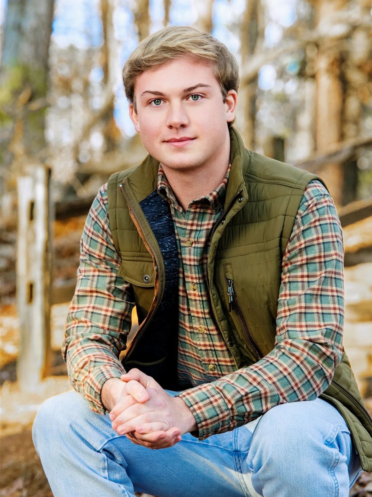 Young man wearing a plaid shirt and olive green vest in a forest