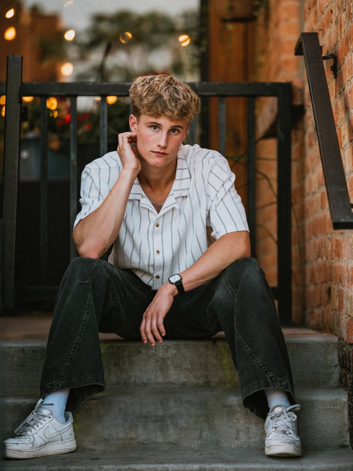 Young man in striped shirt and wide-leg trousers sitting on concrete steps.