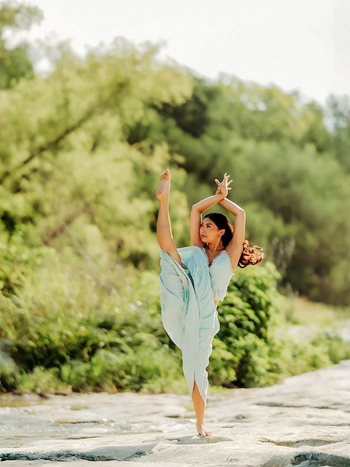 Woman in light blue dress performing a dance pose on rocky ground outdoors