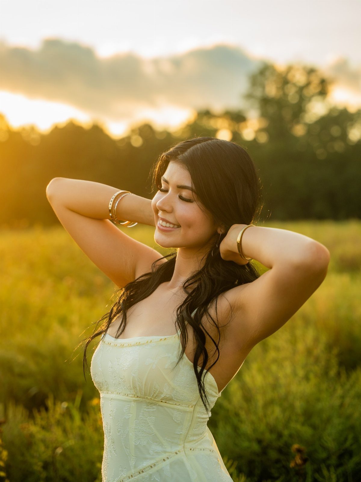 Young woman in yellow dress posing with hands behind head in sunset field
