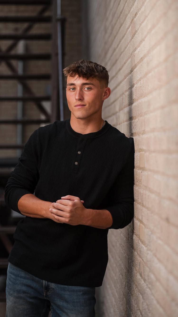 Young man in black shirt leaning against a brick wall with clasped hands
