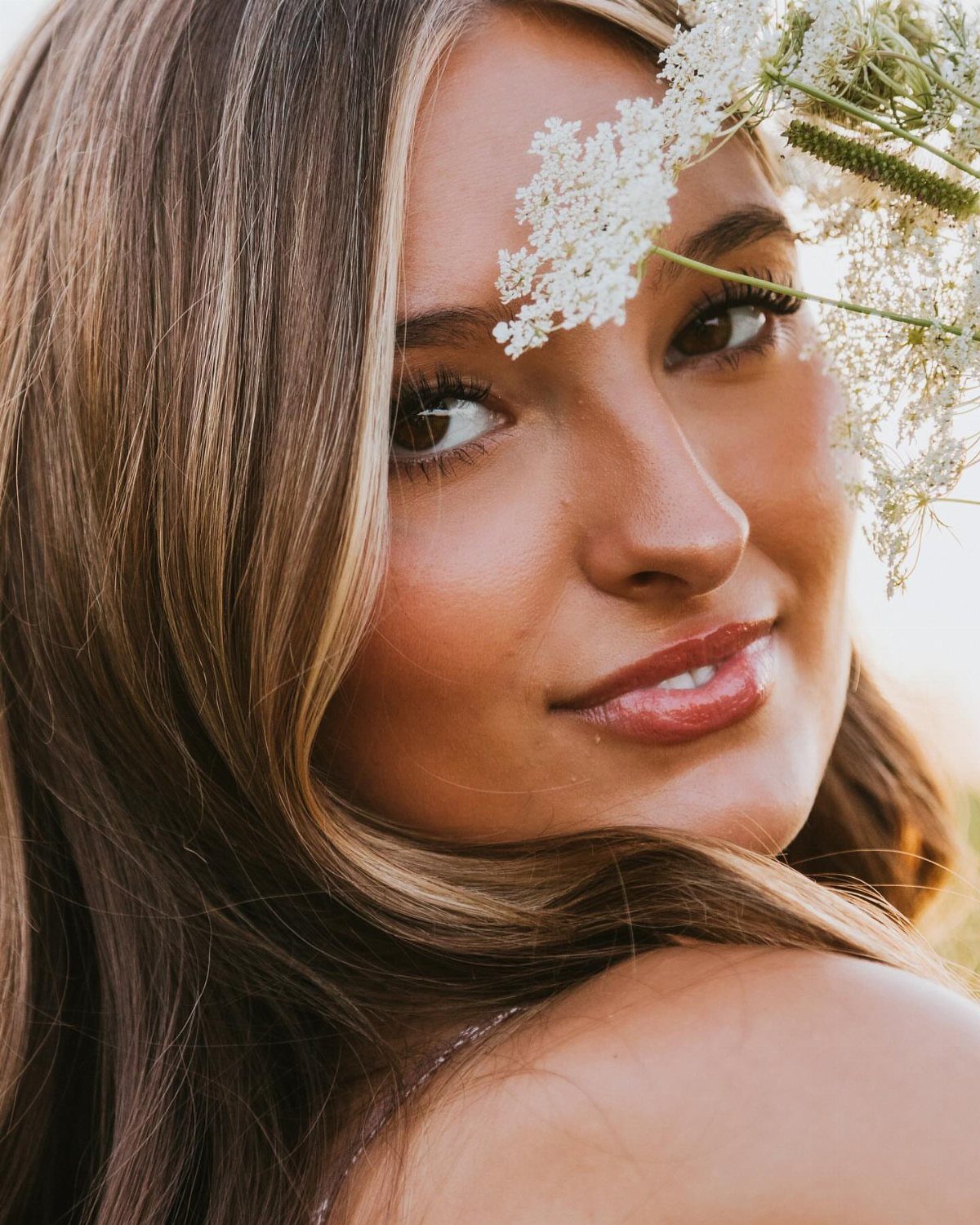 Young woman with highlighted hair posing with white wildflowers in a close-up portrait