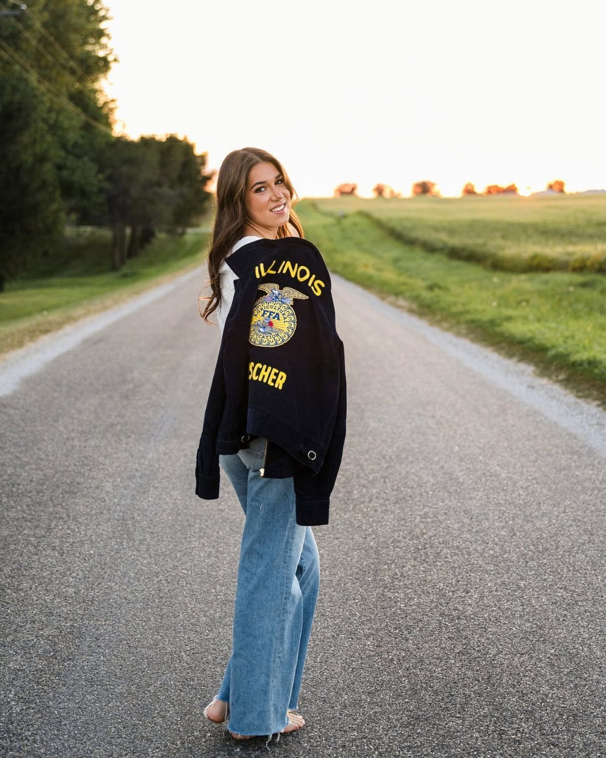 Young woman in a varsity jacket and jeans posing on a rural road