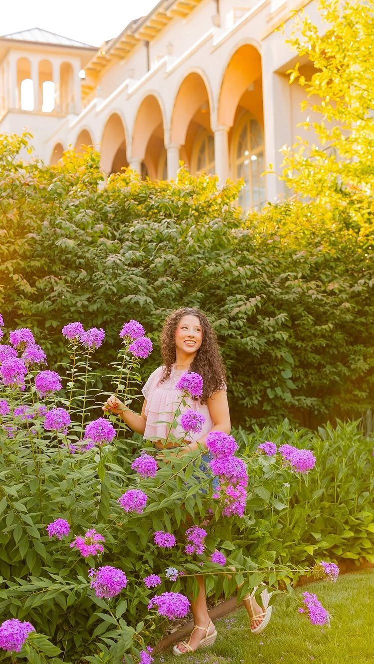 Young woman smiling while standing among tall purple phlox flowers in a garden