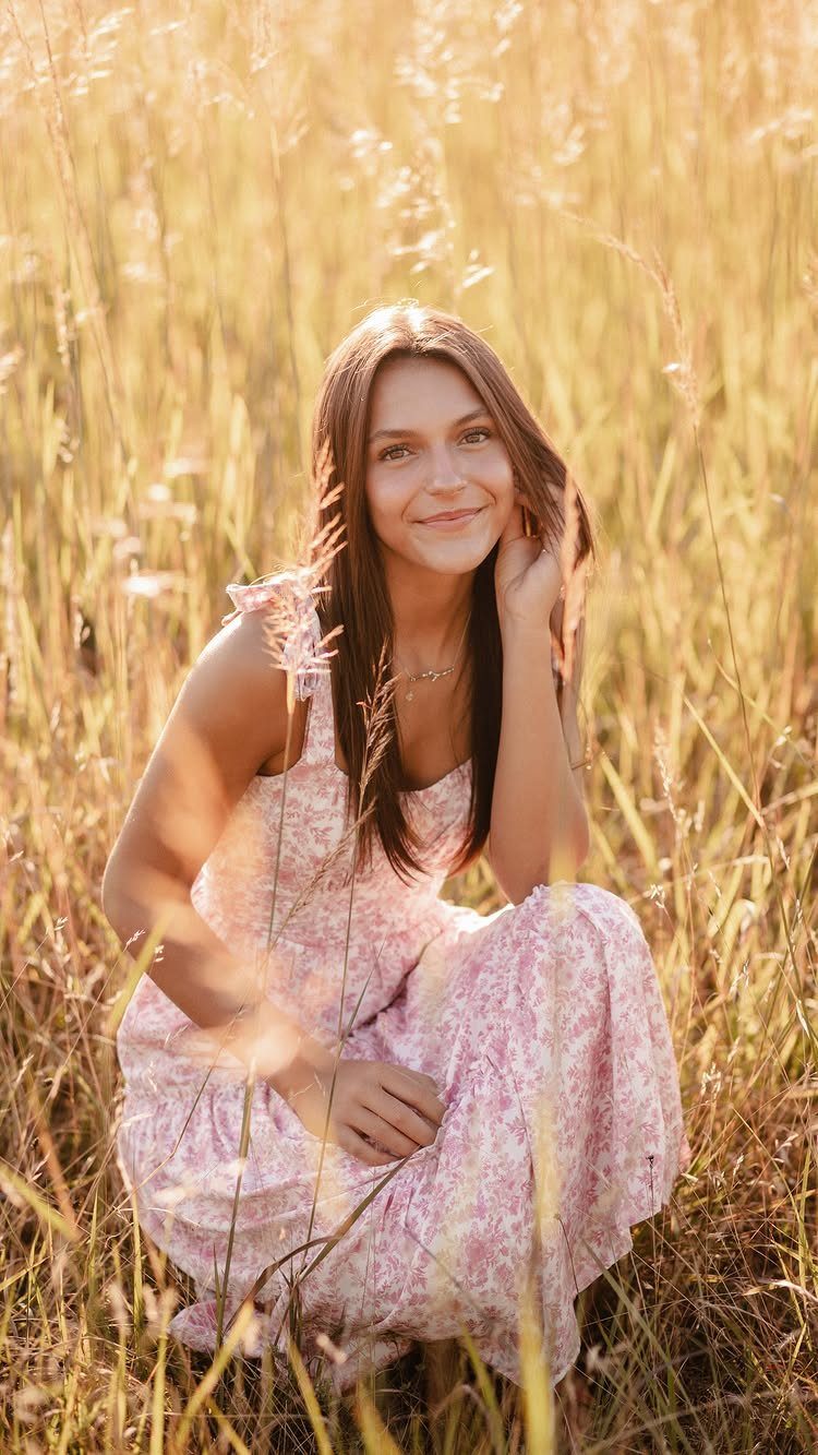 Young woman in pink floral dress crouching in golden grass touching her hair