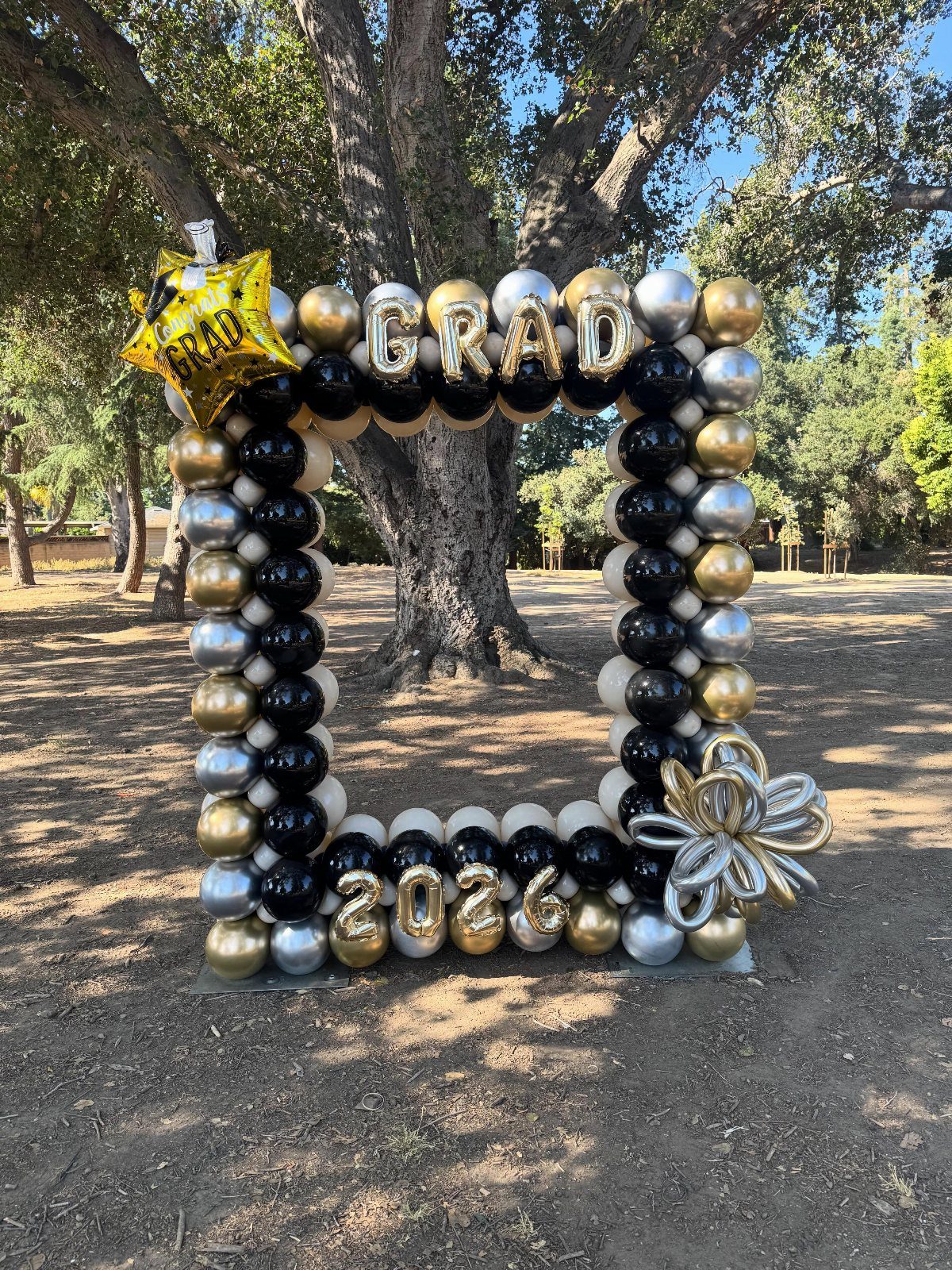 Balloon frame with GRAD and 2026 foil letters standing outdoors under a tree