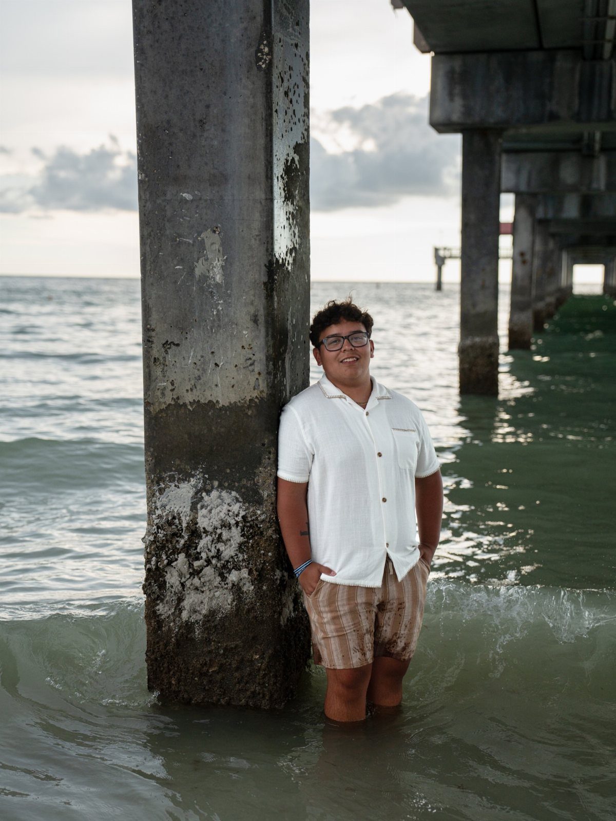 Young man leaning against a concrete pier piling while standing in ocean water.