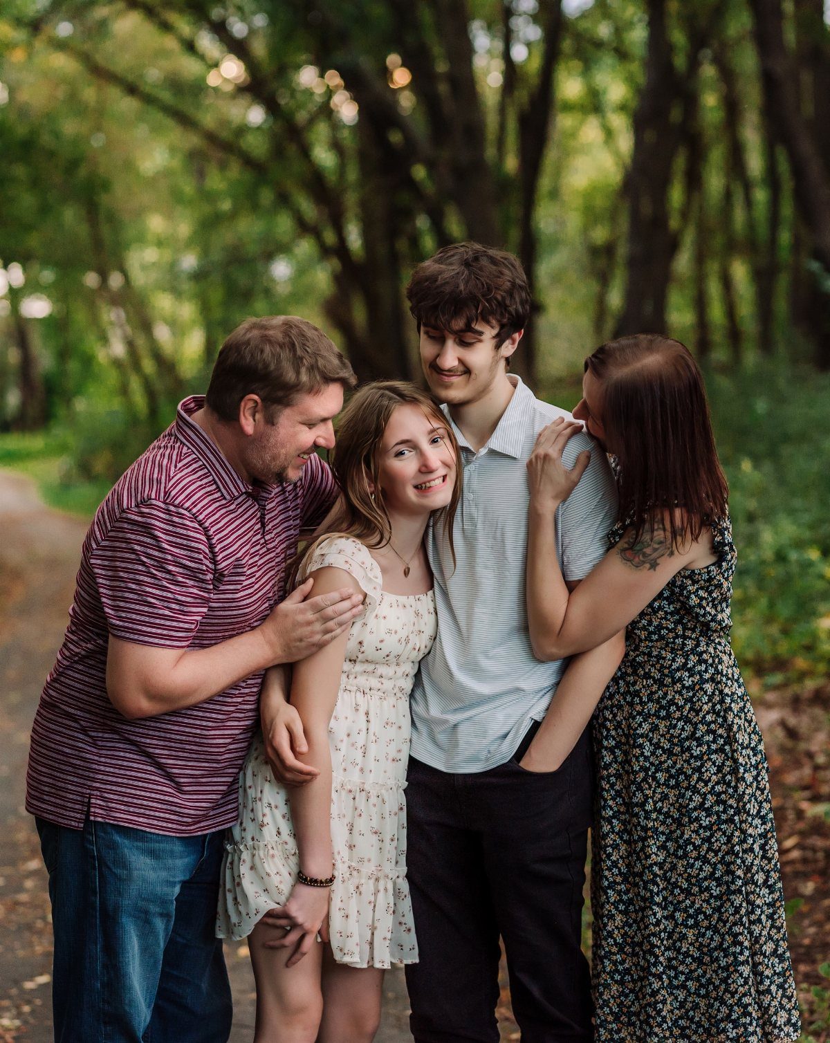 Family of four posing closely together on a path in a green forest.