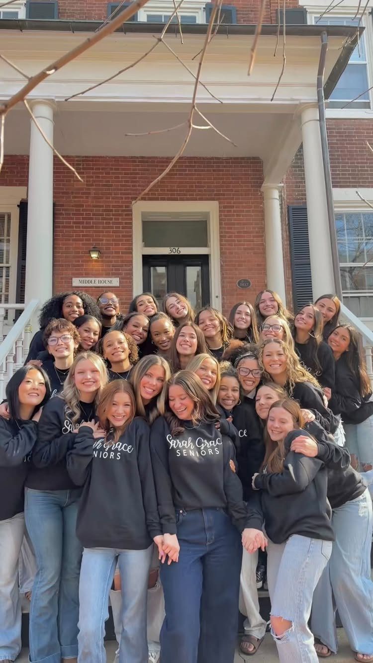 Group of teenage girls in matching black sweatshirts posing on brick building steps.