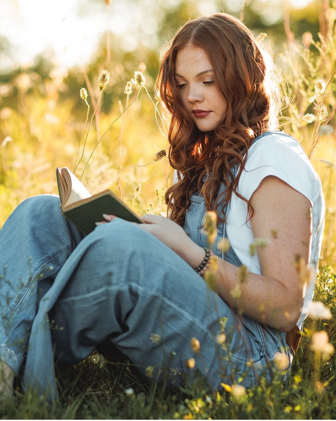 Young woman with red hair reading a book in a sunny grassy field
