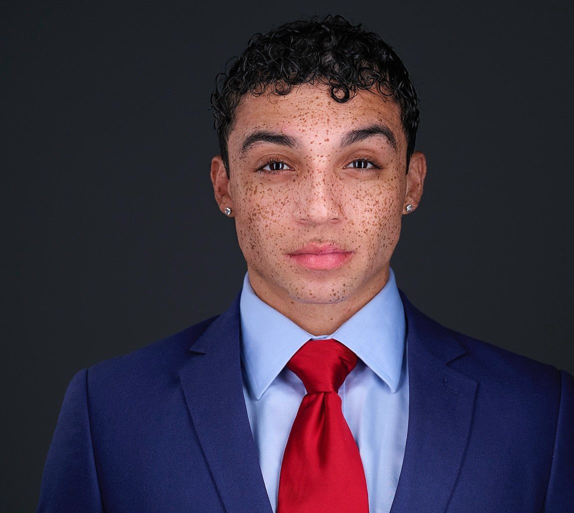 Young man with freckles wearing a blue suit and red tie for a headshot.