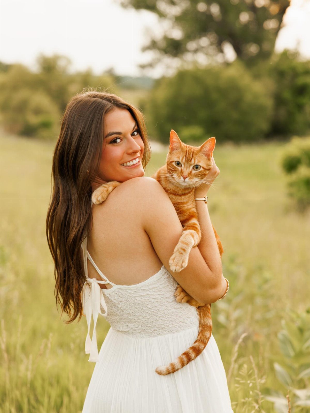 Young woman in a white dress holding an orange tabby cat in a field