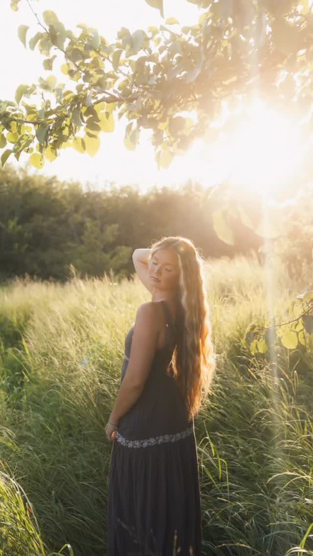 Young woman in a dark dress standing in a sunlit grassy field.
