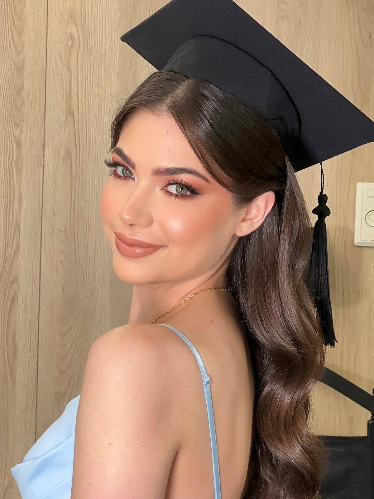 Young woman in a graduation cap and blue dress posing for a portrait