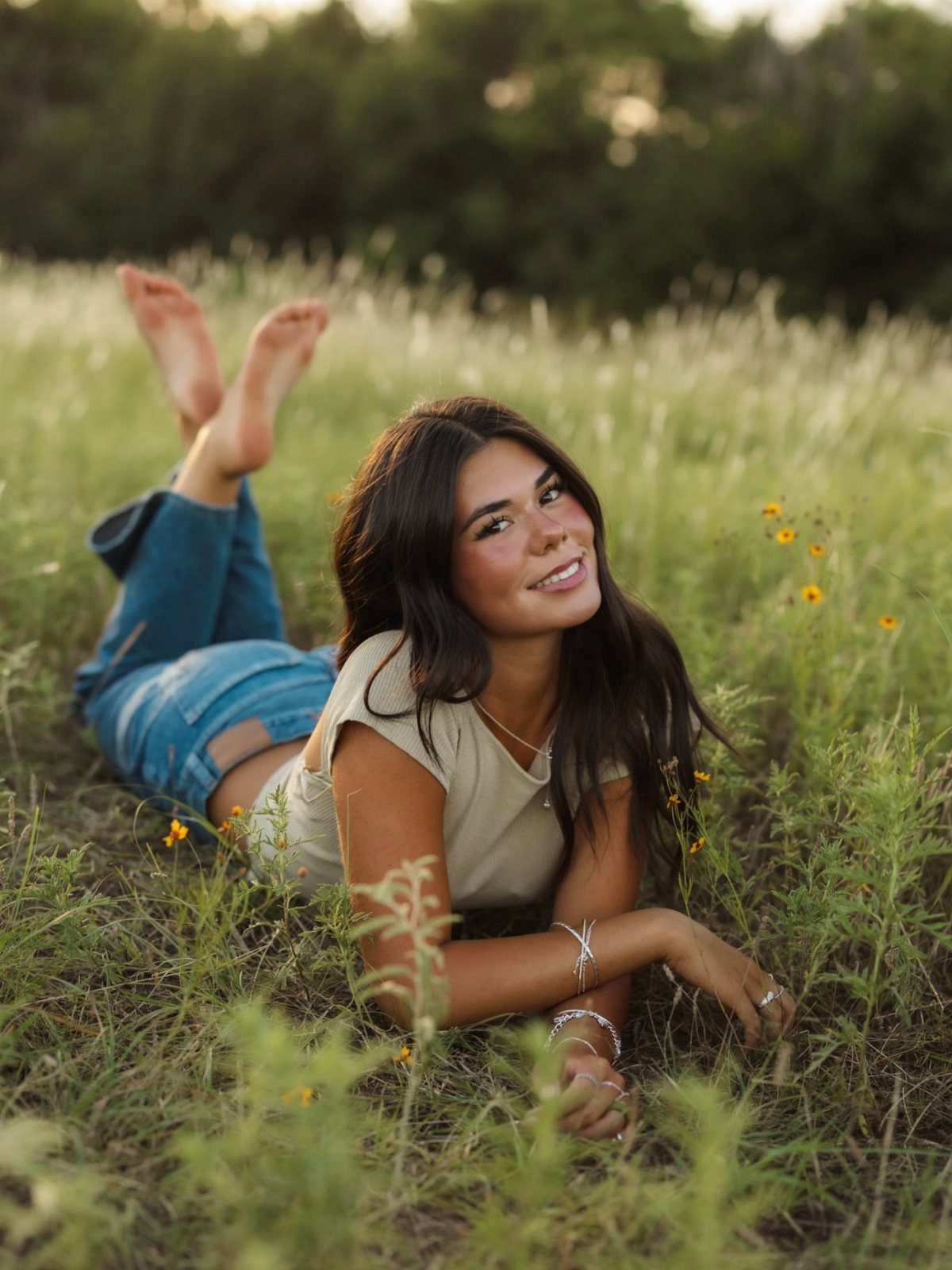 Young woman smiling while lying in a grassy field for senior portraits.