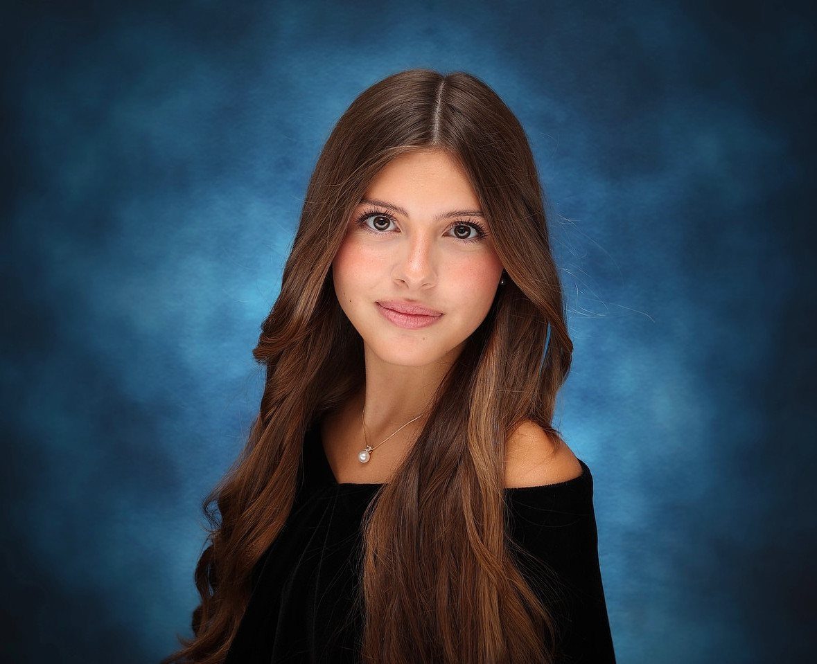 Young woman with long brown hair posing for a studio portrait against blue background