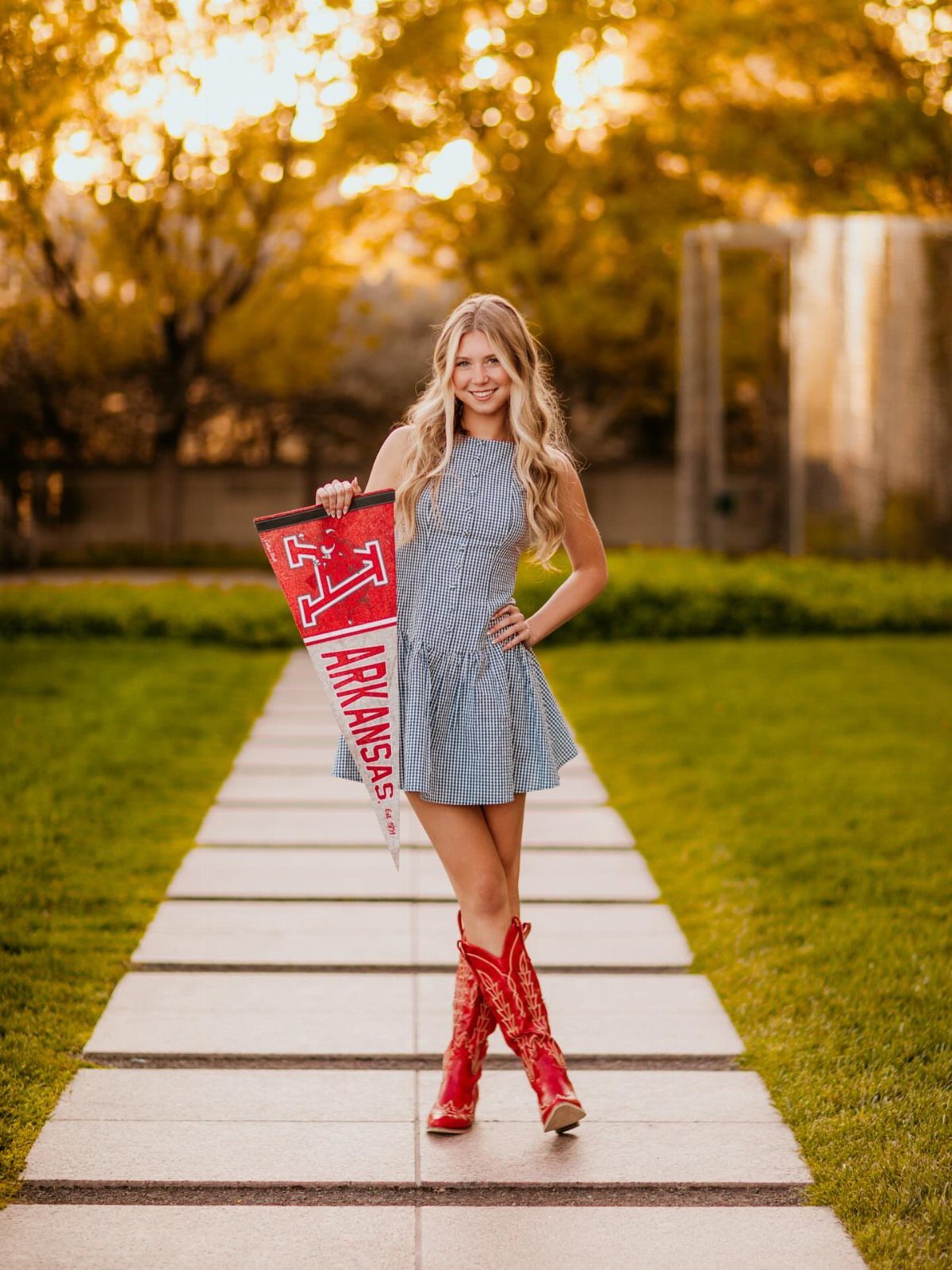 Blonde woman in checkered dress and red boots holding an Arkansas university pennant.