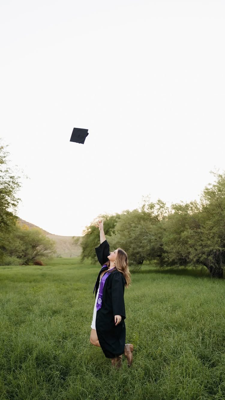 Graduate in black gown tossing her cap into the air in a field