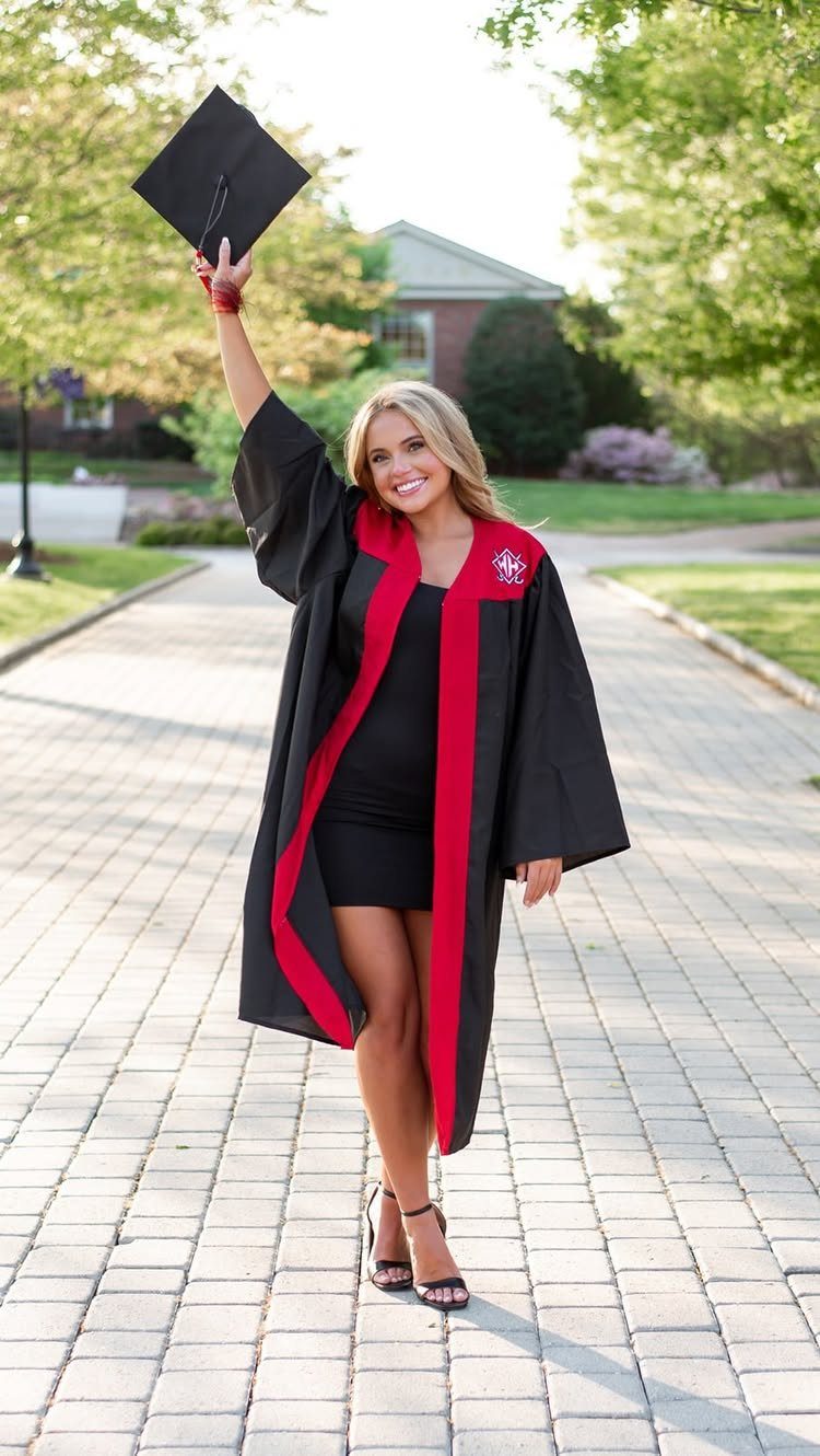 Smiling graduate in black and red gown holding her cap aloft on a walkway