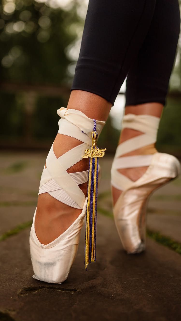 Ballet pointe shoes with a blue and gold 2025 graduation tassel draped over ribbons