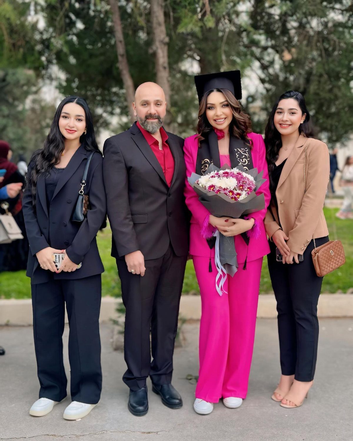 Graduate in pink suit and cap posing with her family outdoors with flowers