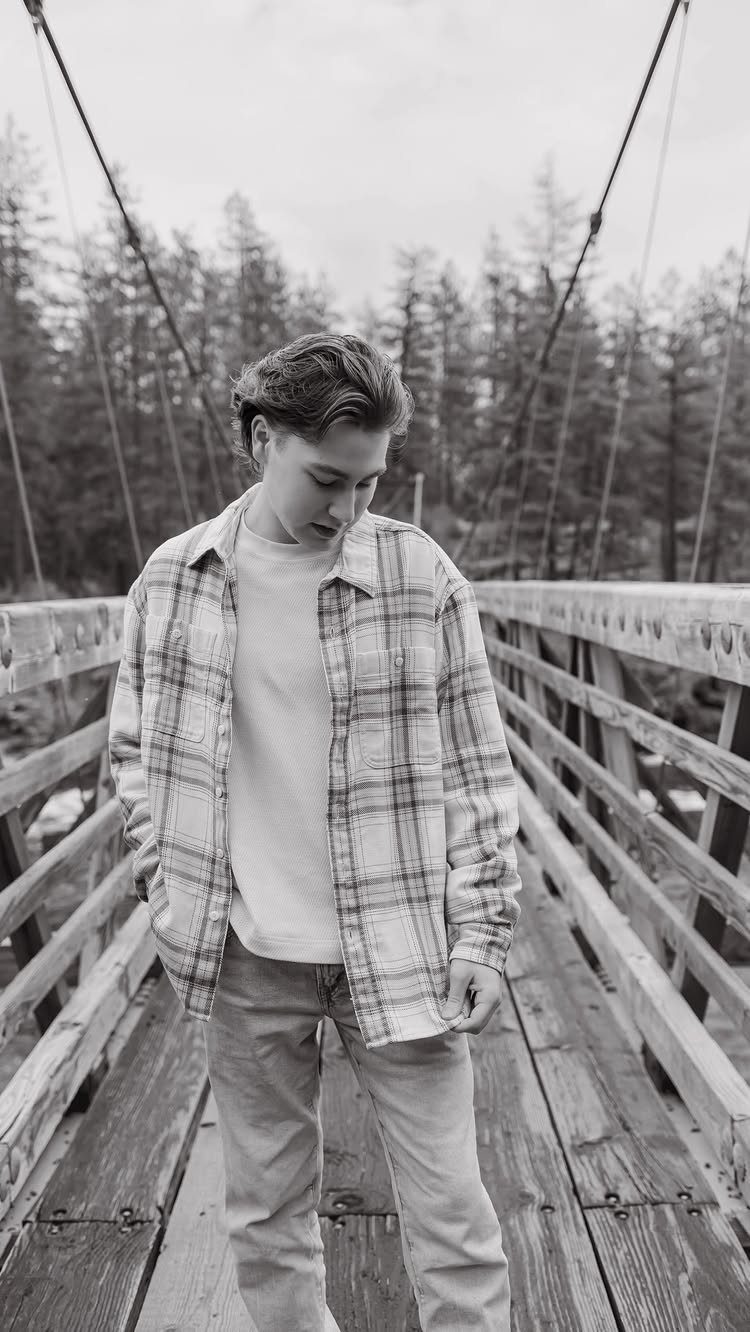 Young man wearing a plaid shirt over a t-shirt on a wooden bridge.