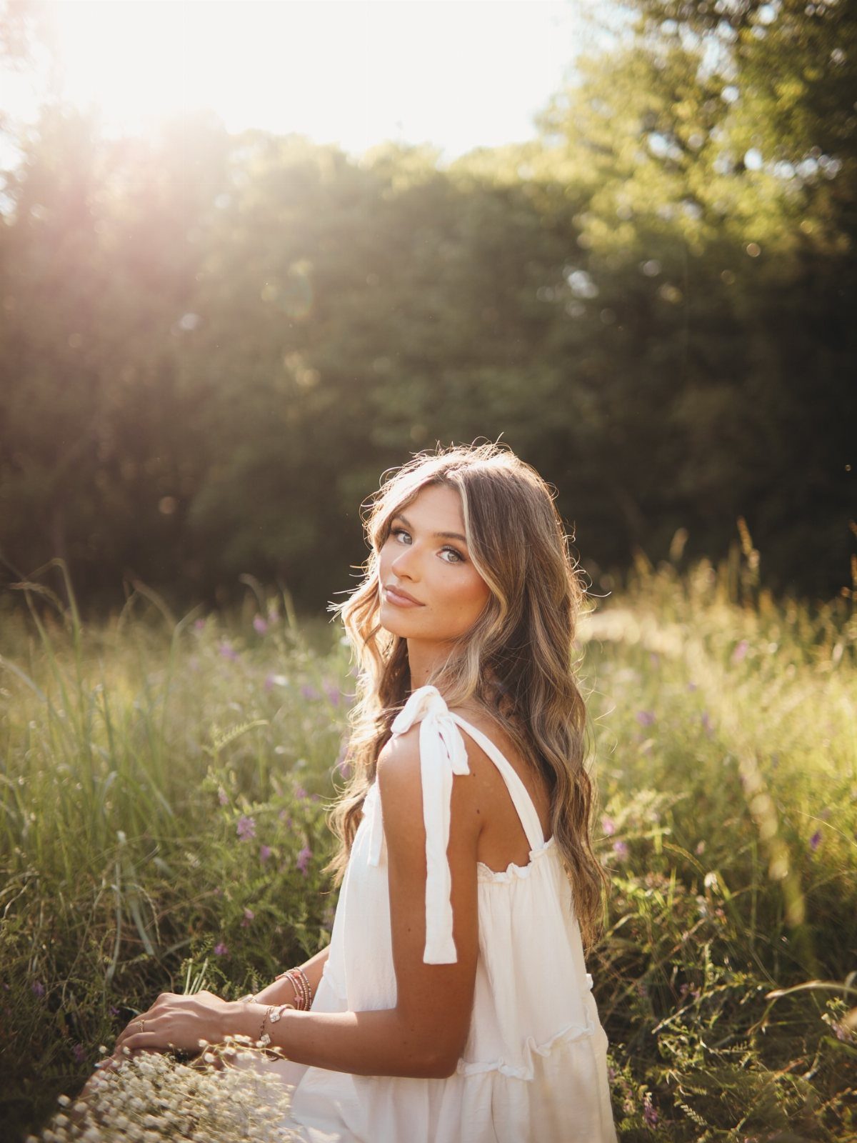 Young woman in a white summer dress posing in a sunny wildflower field