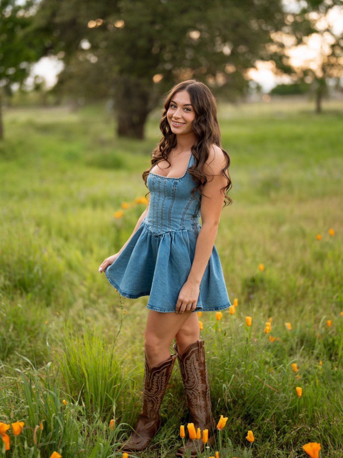 Young woman in a blue denim dress and brown cowboy boots in a field