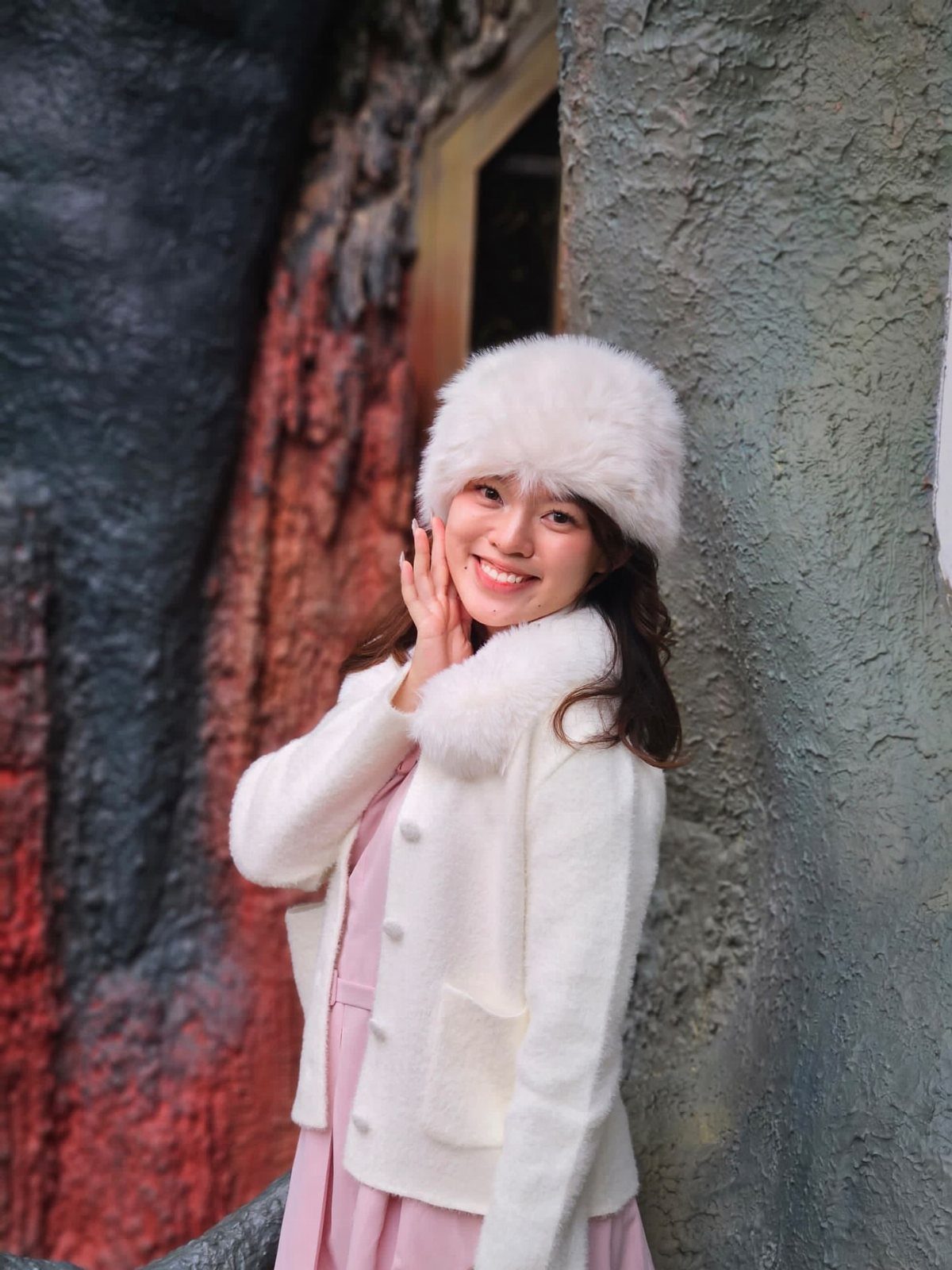 Young woman in white faux fur hat and cardigan with a pink dress.