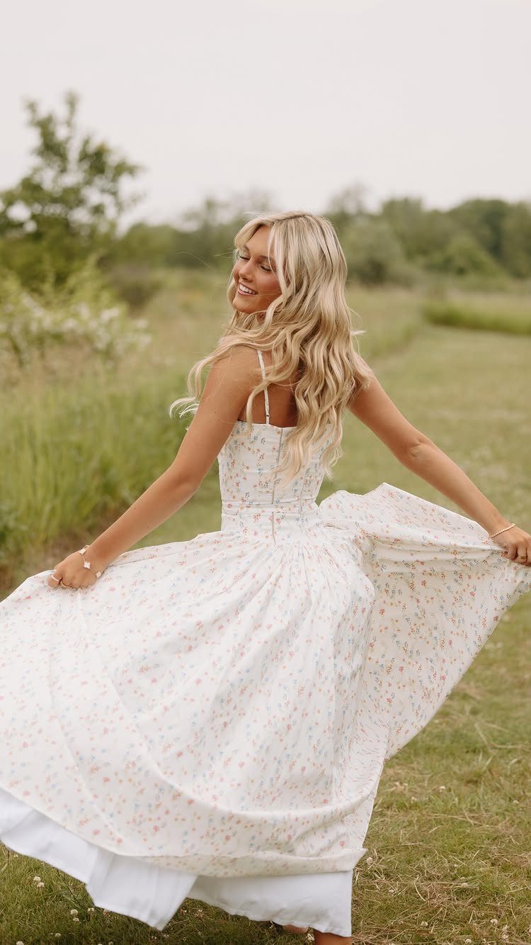 Blonde woman twirling in a white floral maxi dress in a grassy field