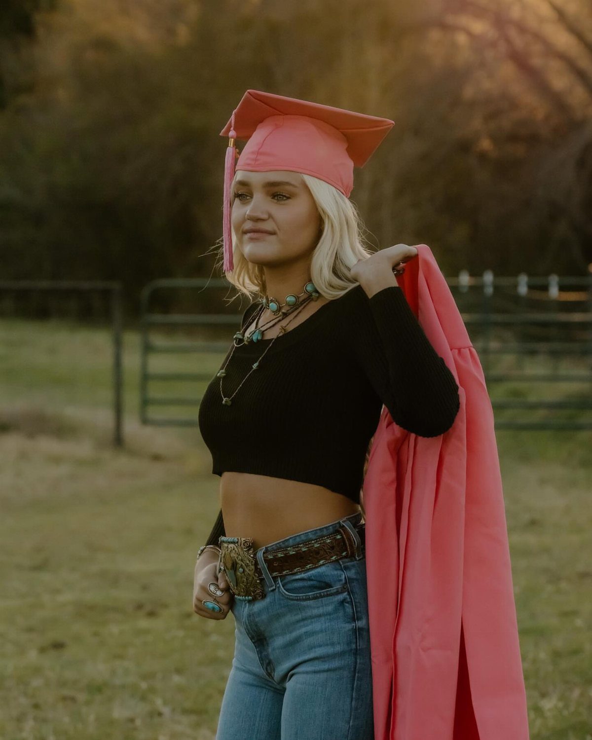 Blonde woman in pink graduation cap and gown wearing turquoise jewelry and belt.