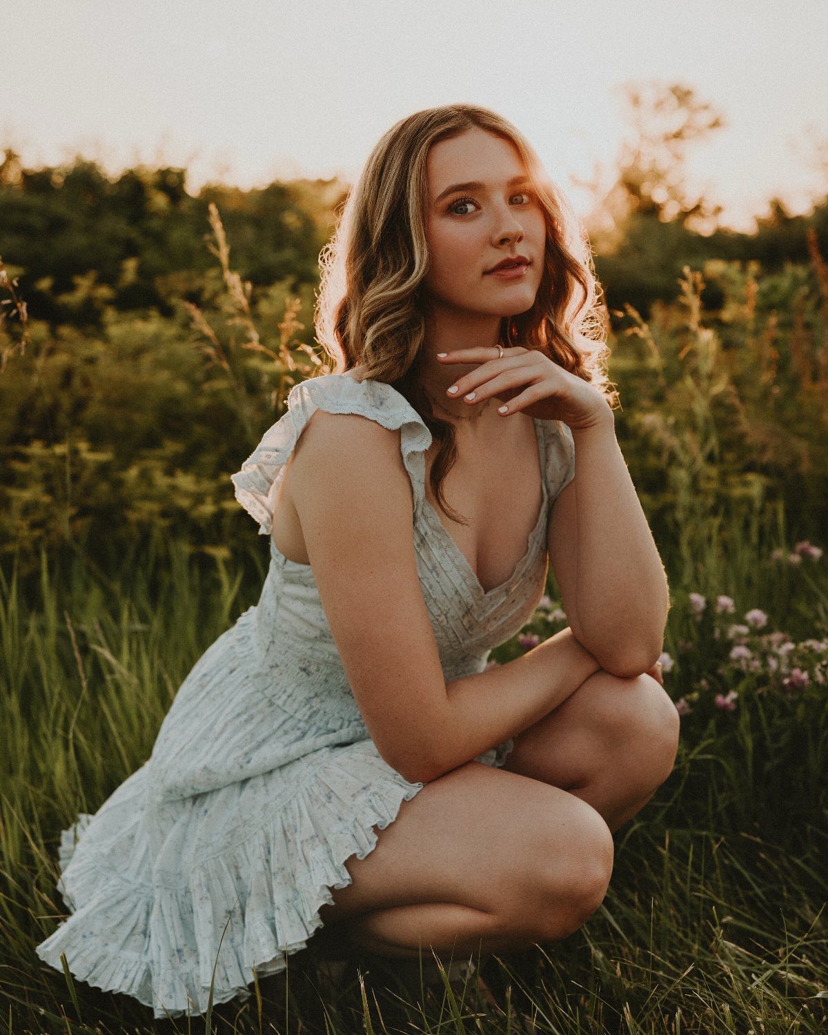 Young woman in a light neutral ruffled dress crouching in a grassy field